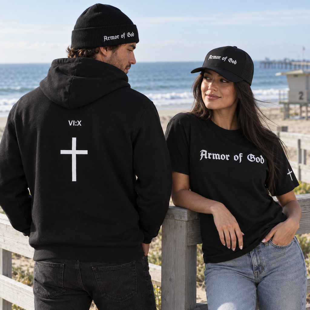 Armor of God cuffed beanie and cross-back hoodie beside a woman wearing the trucker cap and Classic T-Shirt at the coast