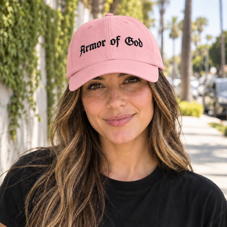 Female model wearing the Armor of God Dad Hat in baby pink with black embroidery